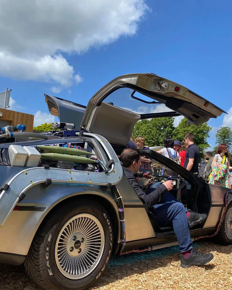 Festival guests gathered around the DeLorean Time Machine with gull-wing doors up — rent for outdoor birthday celebrations