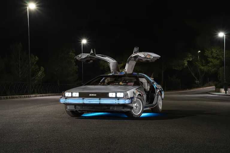 DeLorean Time Machine for hire — front three-quarter view at night with gull-wings up and blue ground lighting