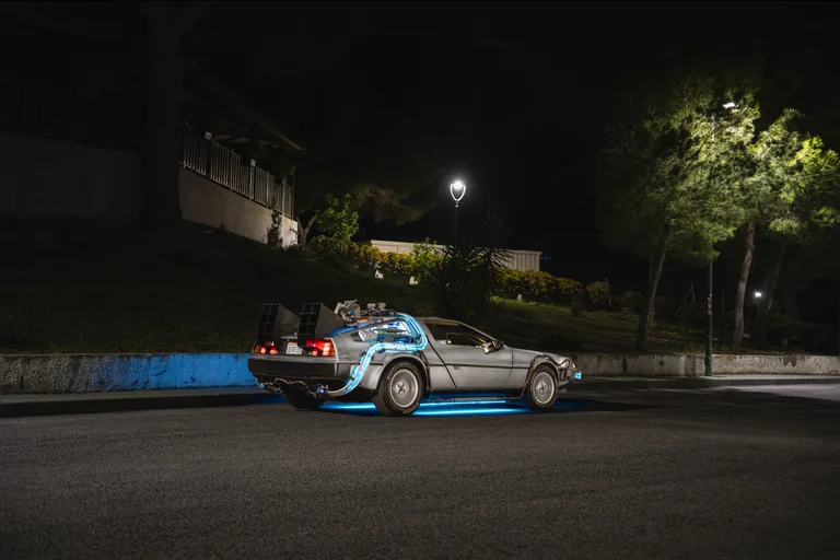 Rear three-quarter shot of the DeLorean Time Machine at night with blue underbody lighting — wedding car hire