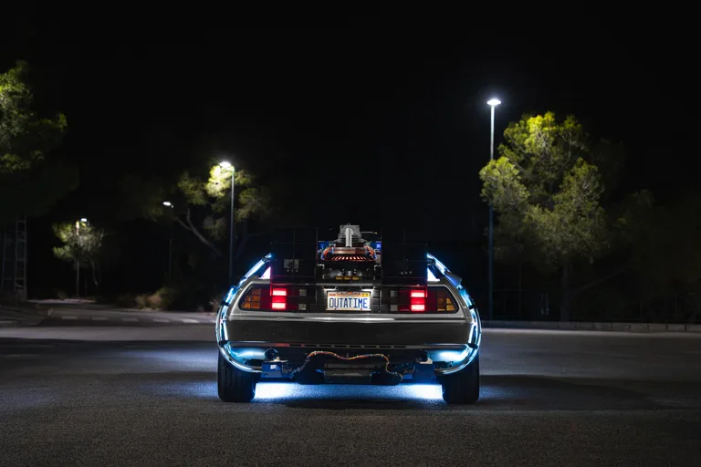 Rear view of the DeLorean Time Machine at night with OUTATIME plate and blue underglow — for hire