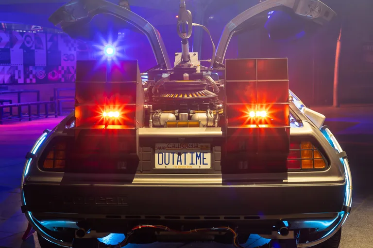 Rear of the DeLorean Time Machine at an event — OUTATIME plate, flashing lights and gull-wing doors raised