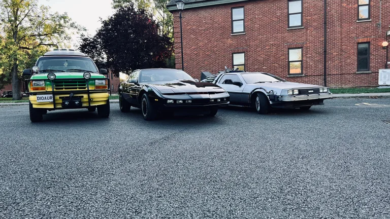 Três carros de cinema lado a lado — o DeLorean do Tempo, o KITT e um Jeep do Parque Jurássico — disponíveis para aluguer