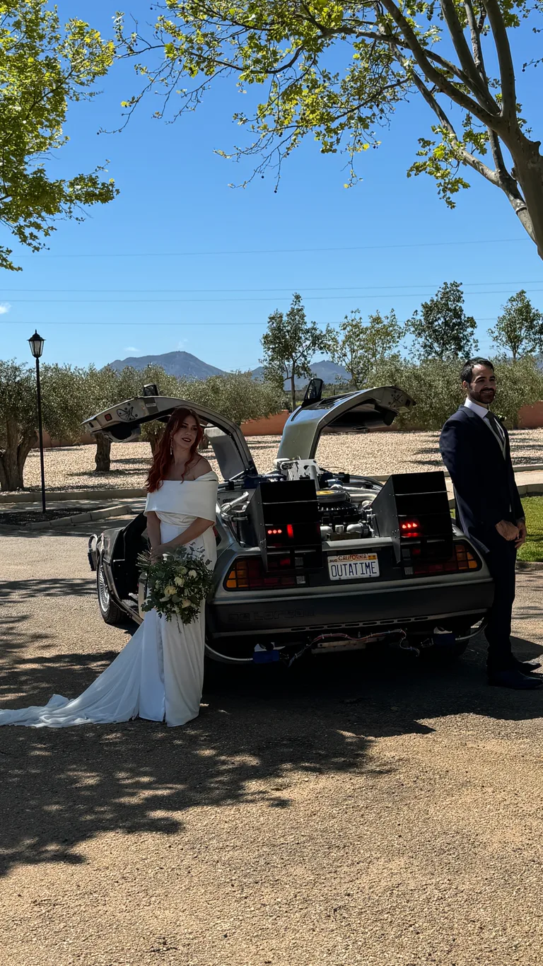 Bride and groom in front of the DeLorean Time Machine at a sunny Spanish estate — wedding car hire across Spain